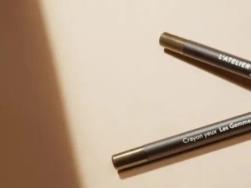 Deux crayons pour les yeux L'Atelier du Sourcil, un avant et un après, sur fond beige.