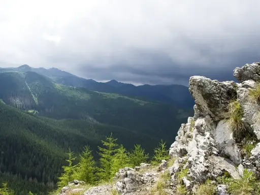Skalisty szczyt w Zakopanem z widokiem na gęsto zalesione doliny Tatr pod burzowym niebem.