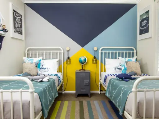 Habitaciones juveniles con camas blancas y pared geométrica en azul, gris y amarillo. Alfombra de rayas y decoración náutica.