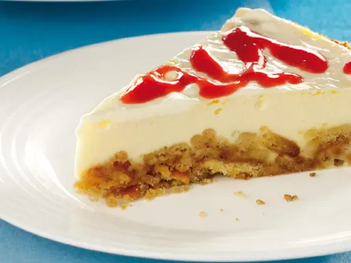 Ein Stück cremiger cheesecake mit keksboden, garniert mit rotem Fruchtpüree auf einem weißen Teller.