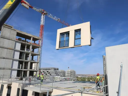 Grúa elevando un módulo prefabricado para la construcción industrializada de un edificio. Obreros supervisan la operación.