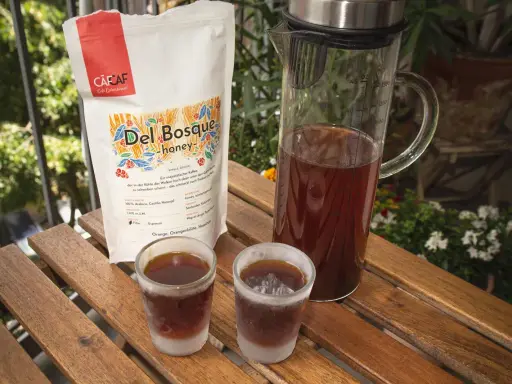 Kalter Kaffee in Gläsern auf Holztisch. Daneben eine Karaffe mit Kaffee und eine Packung "Del Bosque honey". Ein kühler Genuss an einem warmen Tag.