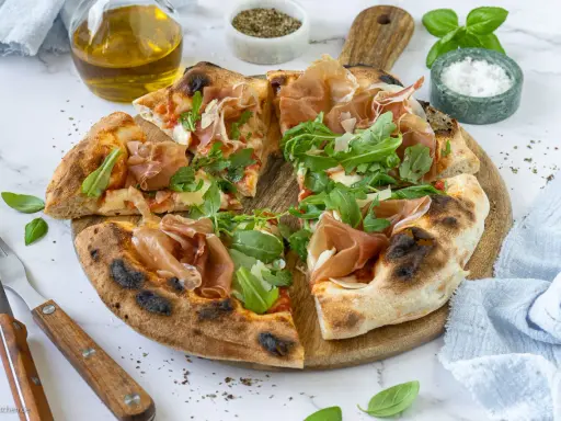 Pizza mit Prosciutto, Rucola und frisch gehobeltem Parmesan. Ein Genuss für alle Sinne!