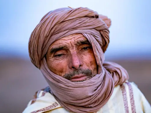 Porträt eines alten Berber Hirtennomaden mit einem Turban und traditioneller Kleidung, dessen Gesicht von der Sonne gezeichnet ist.