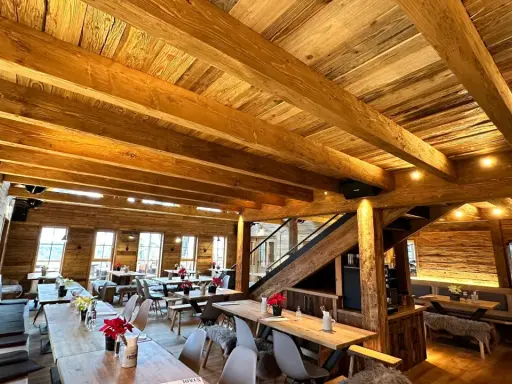 Gemütliches Holzinterieur eines Restaurants mit Holzbalken und Tischen.