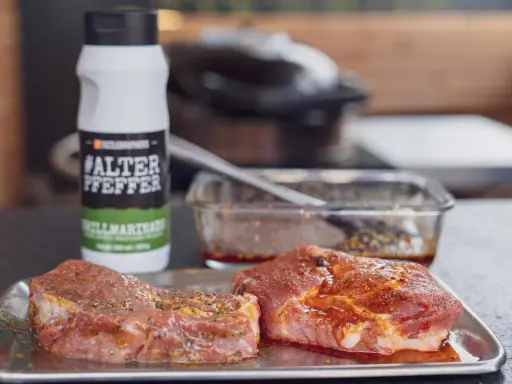 Zwei Steaks liegen auf einem Blech, bereit für die beste Steak Marinade. Daneben eine Flasche "#ALTER PFEPPER" Grillmarinade.