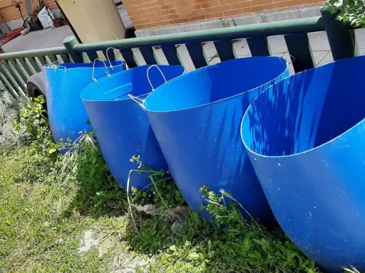 Cuatro grandes barriles azules listos para recoger agua de lluvia en el campo.
