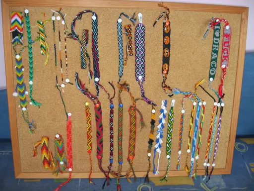 Mnóstwo kolorowych, ręcznie robionych bransoletek na tablicy korkowej. Znajdziesz tu inspirujące pomysły na bransoletki z frędzlami, koralikami i różnymi wzorami.
