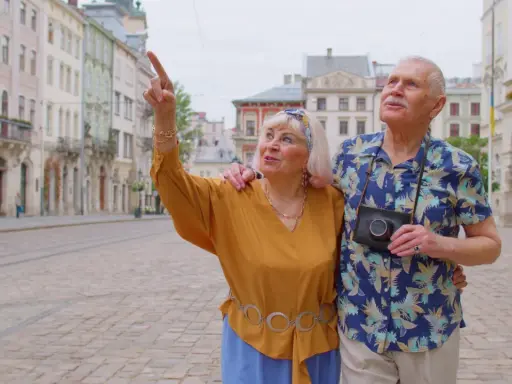 Starsze małżeństwo odkrywa urokliwe, przyjazne seniorom miasta. Kobieta z aparatem wskazuje na zabytkową architekturę.