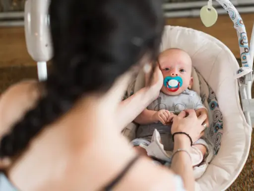 Maluszek w bujaczku polecanym przez fizjoterapeutów. Mama delikatnie głaszcze go po główce, uspokajając.