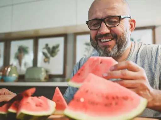 Glücklicher Mann mit Brille isst Wassermelone. Die Wassermelone Nachteile sind, dass sie schnell aufgebraucht ist.