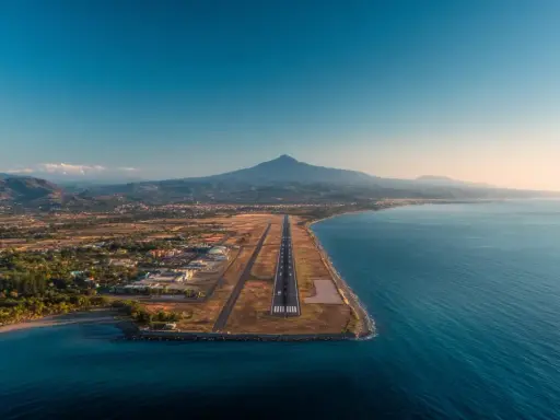 Flygplats vid havet med berg i bakgrunden. En landningsbana sträcker sig ut mot vattnet, en vy som påminner om Palermo flygplats.