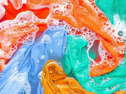 Ropa de color lavadora con burbujas de jabón. Prendas naranjas, azules, verdes y amarillas sumergidas en agua.