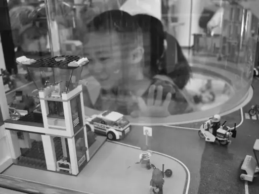 Bambina osserva con stupore un **reportage fotografico** di idee con costruzioni Lego: un commissariato, auto della polizia e personaggi in azione.