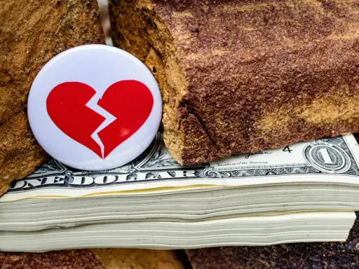 Symbol złamanego serca na stosie dolarów, między kamieniami. Nieoficjalna separacja, gdzie pieniądze dzielą.
