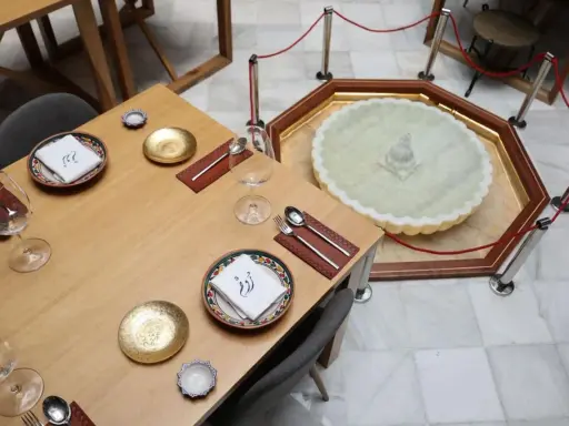 Mesa elegante en el restaurante El Puente El Tejar, con vajilla dorada y una fuente ornamental en el centro.