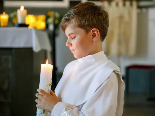Chłopiec w białej albie trzyma zapaloną świecę podczas uroczystości komunii świętej.