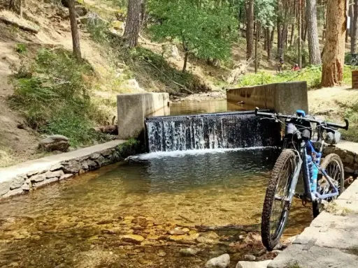 Bicicleta de montaña junto a una cascada en un arroyo, ideal para rutas por Segovia.
