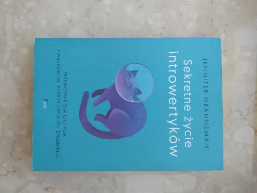 Książka "Sekretne życie introwertyków" z kotem w hełmie kosmicznym. Przewodnik dla cichych i tych, którzy chcą ich zrozumieć.