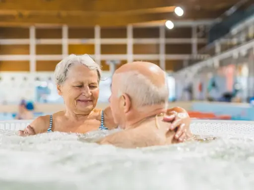 Uśmiechnięta para seniorów relaksuje się w jacuzzi w basenie. To wspaniałe miejsce, jak sanatorium szpitalne, gdzie można odzyskać siły.