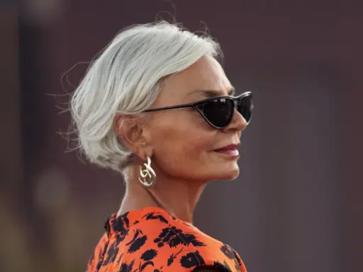 Elegante Frau mit Kurzhaarfrisur ab 60, Sonnenbrille und auffälligem Ohrring.