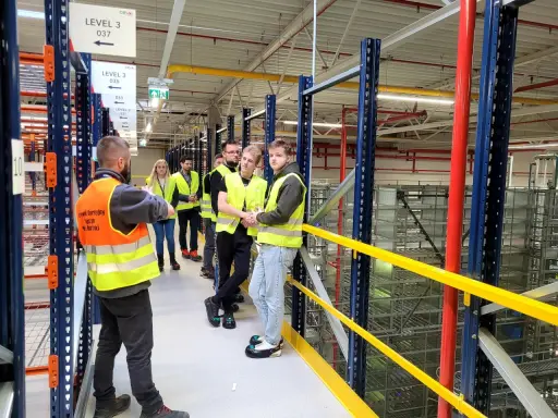Grupa osób w kamizelkach odblaskowych zwiedza magazyn CEVA Logistics. To potencjalna ceva logistics praca.