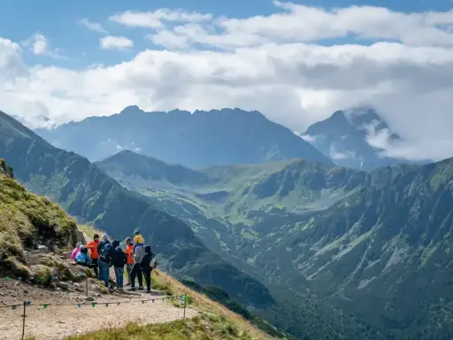 Grupa turystów odpoczywa na szlaku z widokiem na majestatyczne Tatry. W oddali majaczy Kasprowy Wierch, otoczony chmurami.