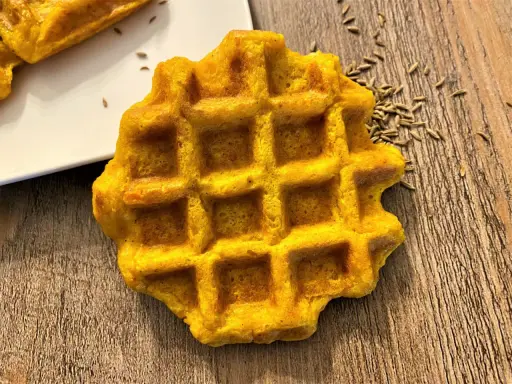 Gaufre carotte dorée, parsemée de graines sur fond de bois. Un délice orangé à déguster.