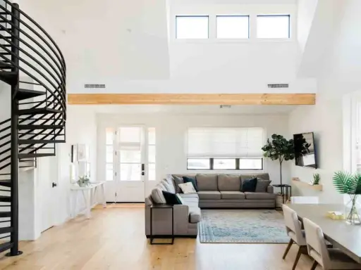 Ampio soggiorno con scala a chiocciola nera, divano angolare grigio e trave in legno a vista. Loft idee originali per un ambiente moderno.