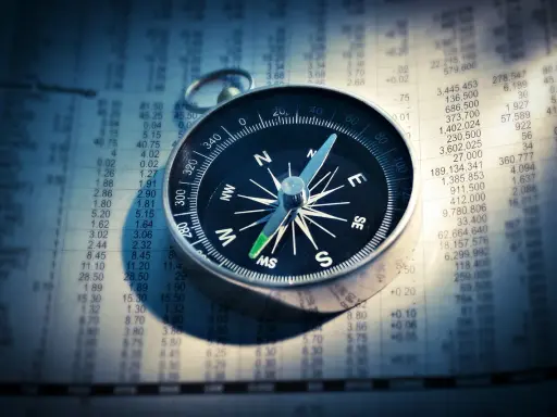 Kompas w telefonie wskazuje kierunek na tle wykresu finansowego.