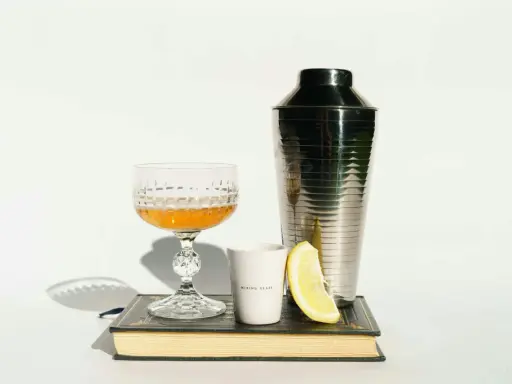 Szklanka z drinkiem, shaker, cytryna i książka. Idealne akcesoria, by dowiedzieć się, z czym pić amarula.
