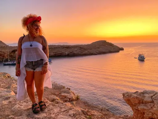 Ragazza con foulard rosso e top bianco, shorts di jeans e sandali, con tramonto spettacolare su Ibiza. L'outfit perfetto per come vestirsi a Ibiza.