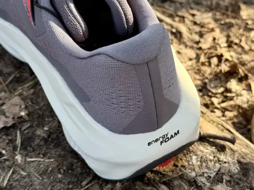 Szary but Salomon Ultra Glide 3 z białą podeszwą i napisem "energy FOAM" na tle leśnej ściółki.