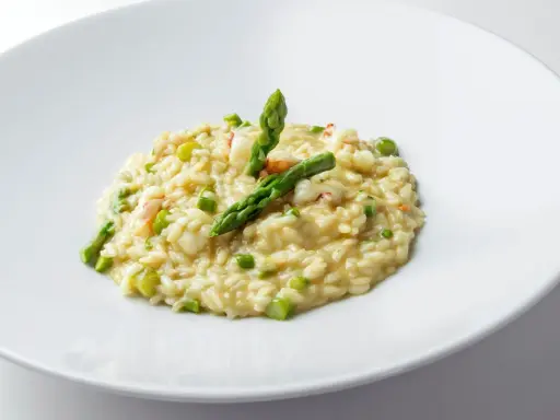 Risotto cremoso con asparagi freschi e succulenti gamberetti, guarnito con punte di asparagi croccanti.
