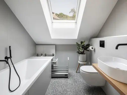 Un piccolo bagno sottotetto basso con vasca, WC, lavabo e lucernario.