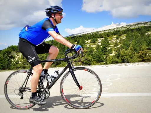Ciclista in maglia blu affronta la **salita** del **Mont Ventoux**, con la cima innevata in lontananza.