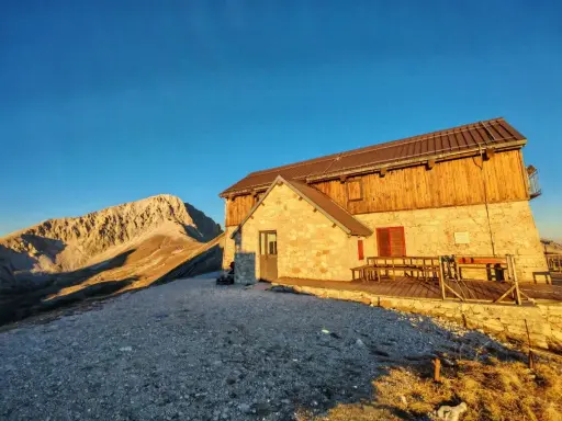 Il rifugio Duca degli Abruzzi, con la sua struttura in pietra e legno, si erge maestoso al tramonto, dominando un paesaggio montano aspro e solitario.