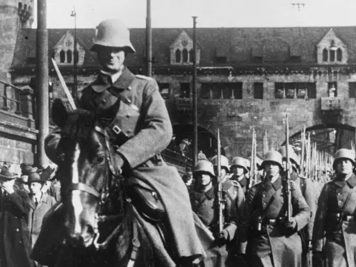 Soldaten marschieren in Formation, ein Reiter führt sie an. Ein historisches Bild der Rheinlandbesetzung 1936.
