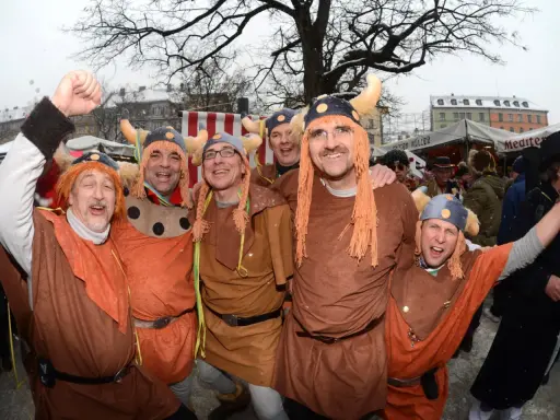 Fröhliche Männer in historischer Wikinger-Kleidung mit Hörnerhelmen und orangefarbenen Perücken feiern ausgelassen.