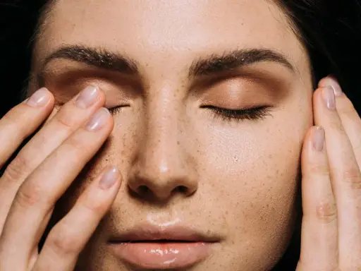 Primo piano di una donna con lentiggini, che si tocca il viso. Potrebbe indicare sintomi di carenza vitamina d sulla pelle.