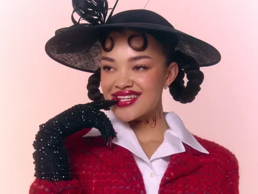 Daniela Rathana med en svart hatt och röd kavaj, med glittriga handskar och en lekfull blick.