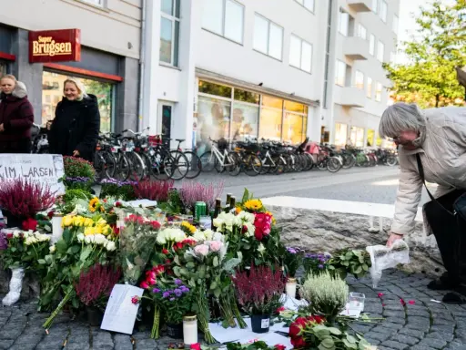 En kvinna lägger blommor vid en minnesplats för Kim Larsen. Många blommor och ljus.