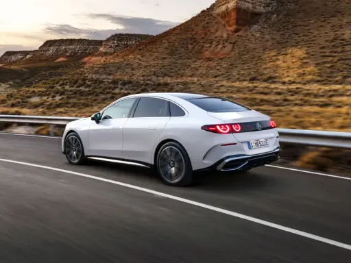 Weißer Mercedes C-Klasse EQ fährt auf einer Straße in bergiger Landschaft.