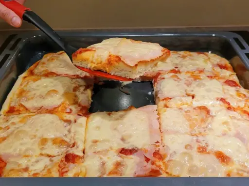 Ania gotuje pizzę. Gorąca, domowa pizza z serem i szynką, właśnie wyjęta z blachy.