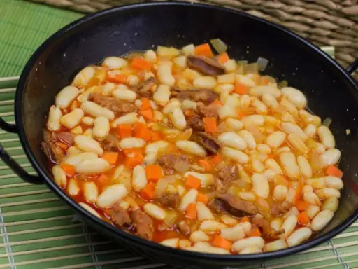 Alubias con chorizo y verduras en una paellera, plato tradicional español.