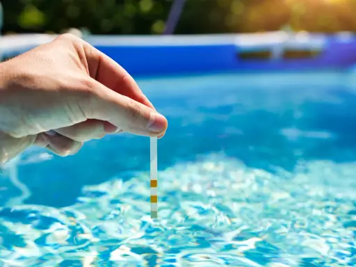 Main tenue une bandelette de test dans l'eau d'une piscine pour vérifier la qualité de l'eau, essentielle au bon fonctionnement du système pompe piscine.