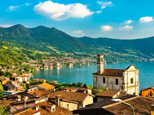 Un borgo pittoresco sul lago, ideale per gite in giornata da Milano. Case con tetti rossi, una chiesa e montagne verdi sullo sfondo.