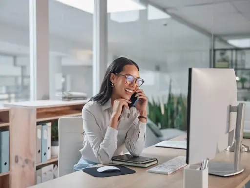 Sorride al telefono, una segretaria part time mattina, mentre lavora al computer in un ufficio moderno.