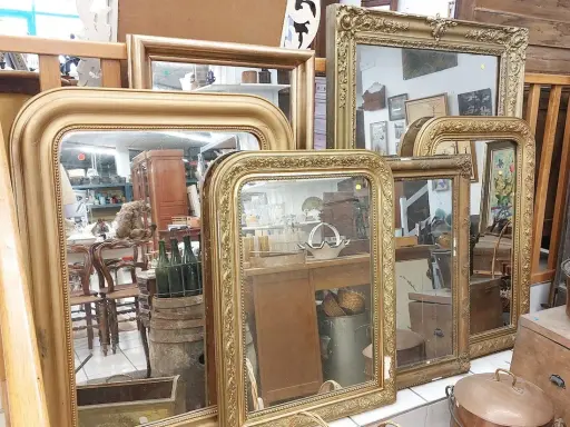 Plusieurs miroirs dorés, certains avec des cadres ornés, sont alignés. Comment reconnaître un miroir Napoléon III ? Cherchez les moulures riches et les détails sculptés.
