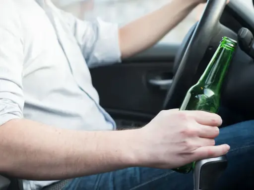 Mężczyzna za kierownicą trzyma butelkę piwa, zastanawiając się, ile promili ma jedno piwo.